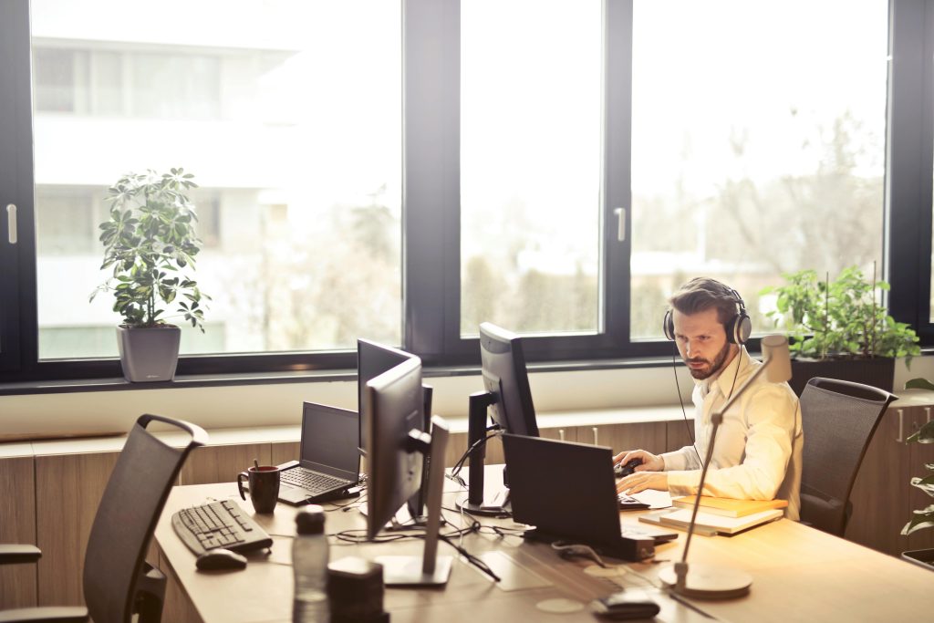 pexels-photo-845451-845451 A businessman sits at a desk using multiple computers and a headset in a well-lit modern office.